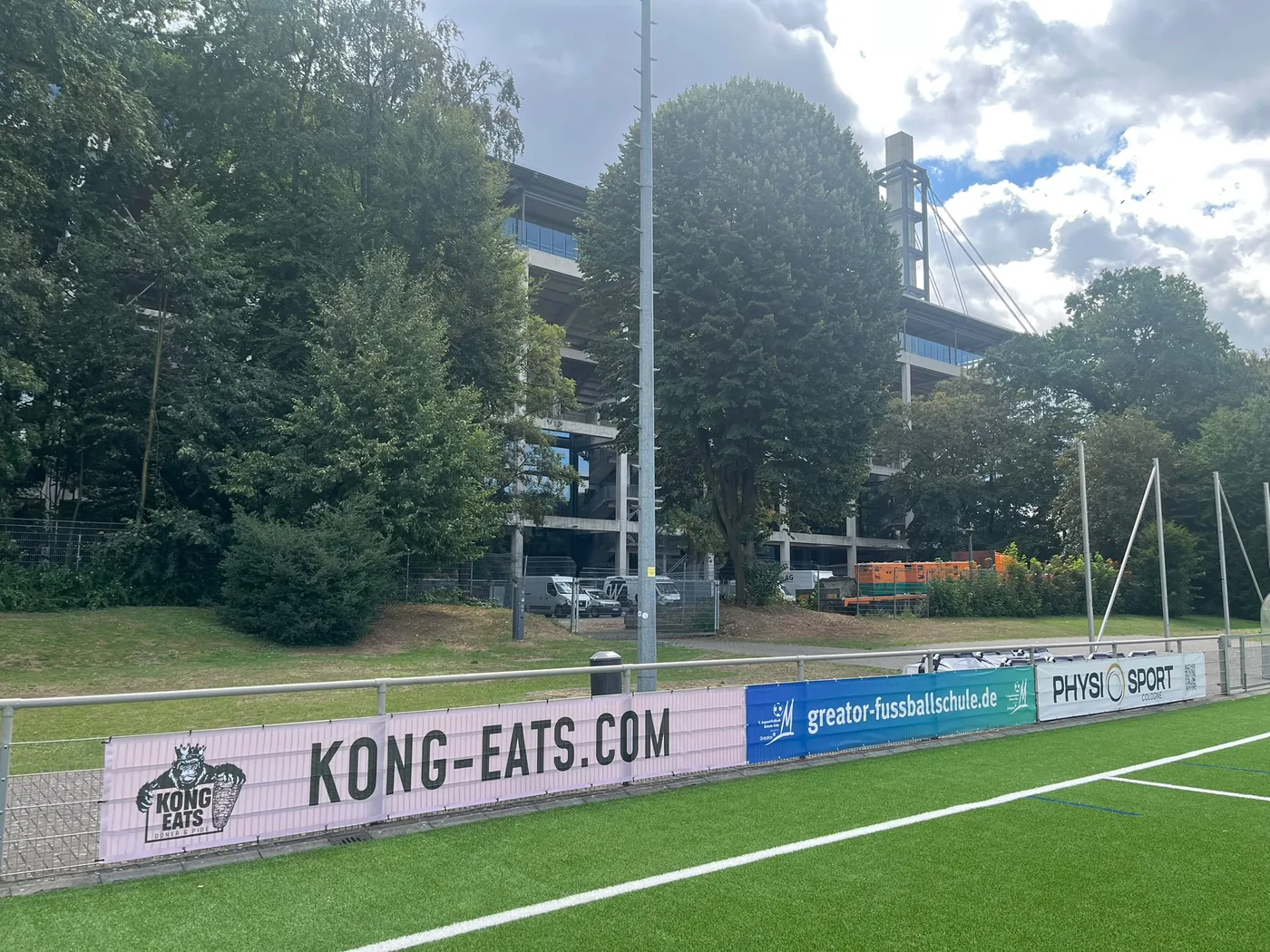 KongEats-Bande am Platz der 1. Jugend-Fußball-Schule Köln, dahinter das RheinEnergieStadion